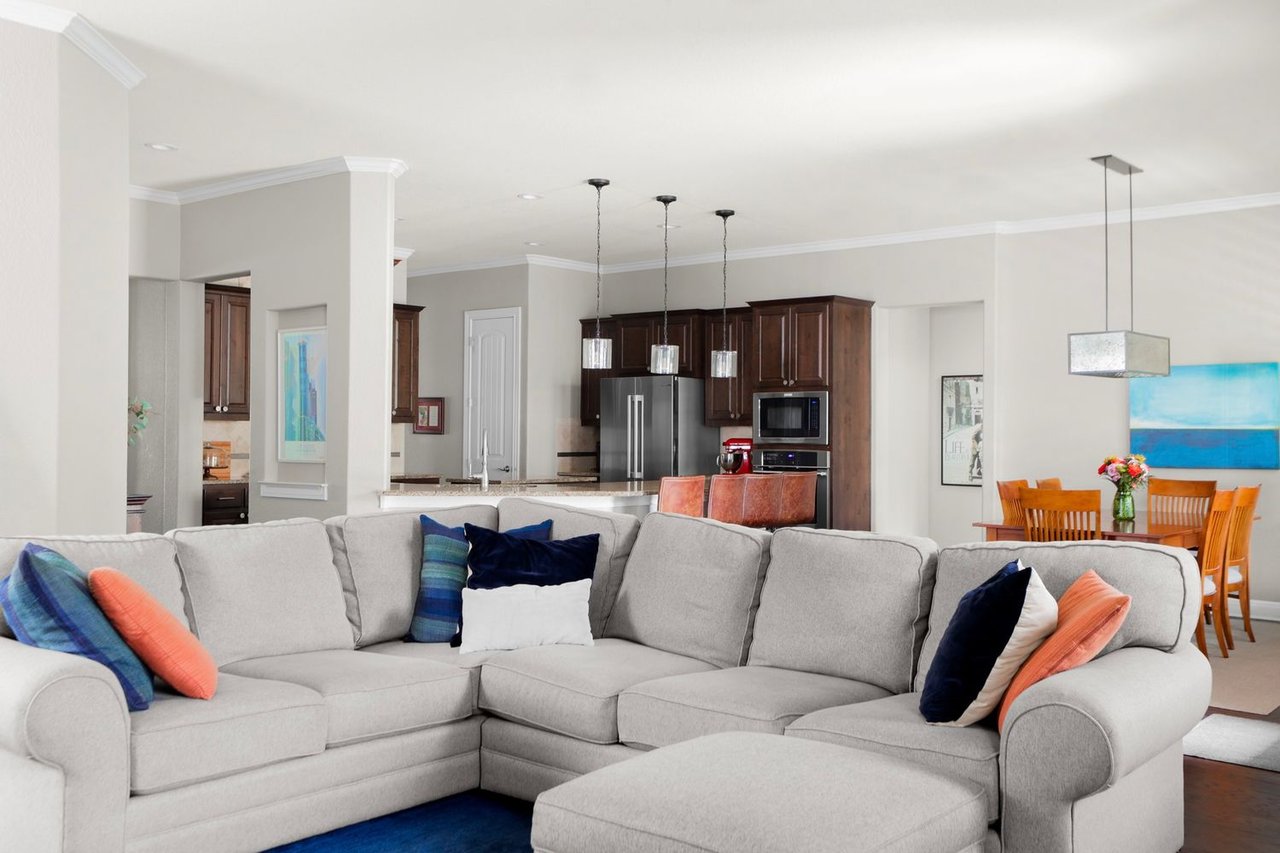 Open-plan living room with a large gray sectional, dark wood kitchen cabinets, and dining area.