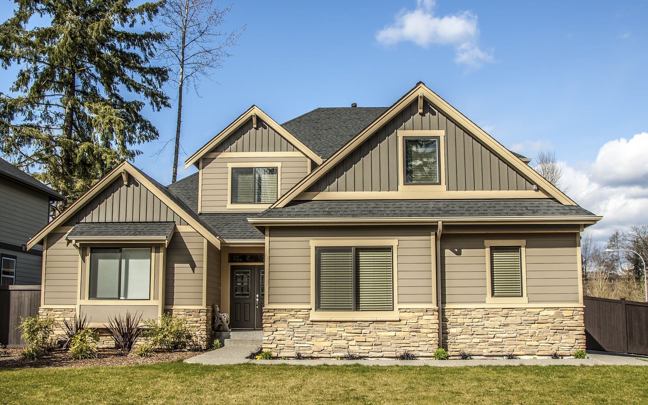 Beige two-story house with stone veneer, multiple gables, and a landscaped front lawn.