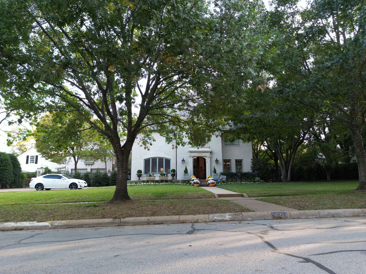 White brick two-story home framed by mature trees, with a broad lawn and decorated front entrance.
