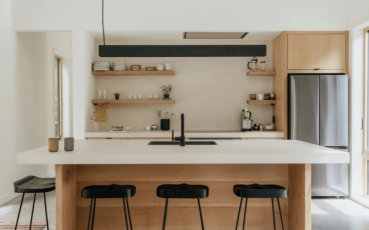 Modern kitchen with a broad white island, light oak cabinetry, and black bar stools.