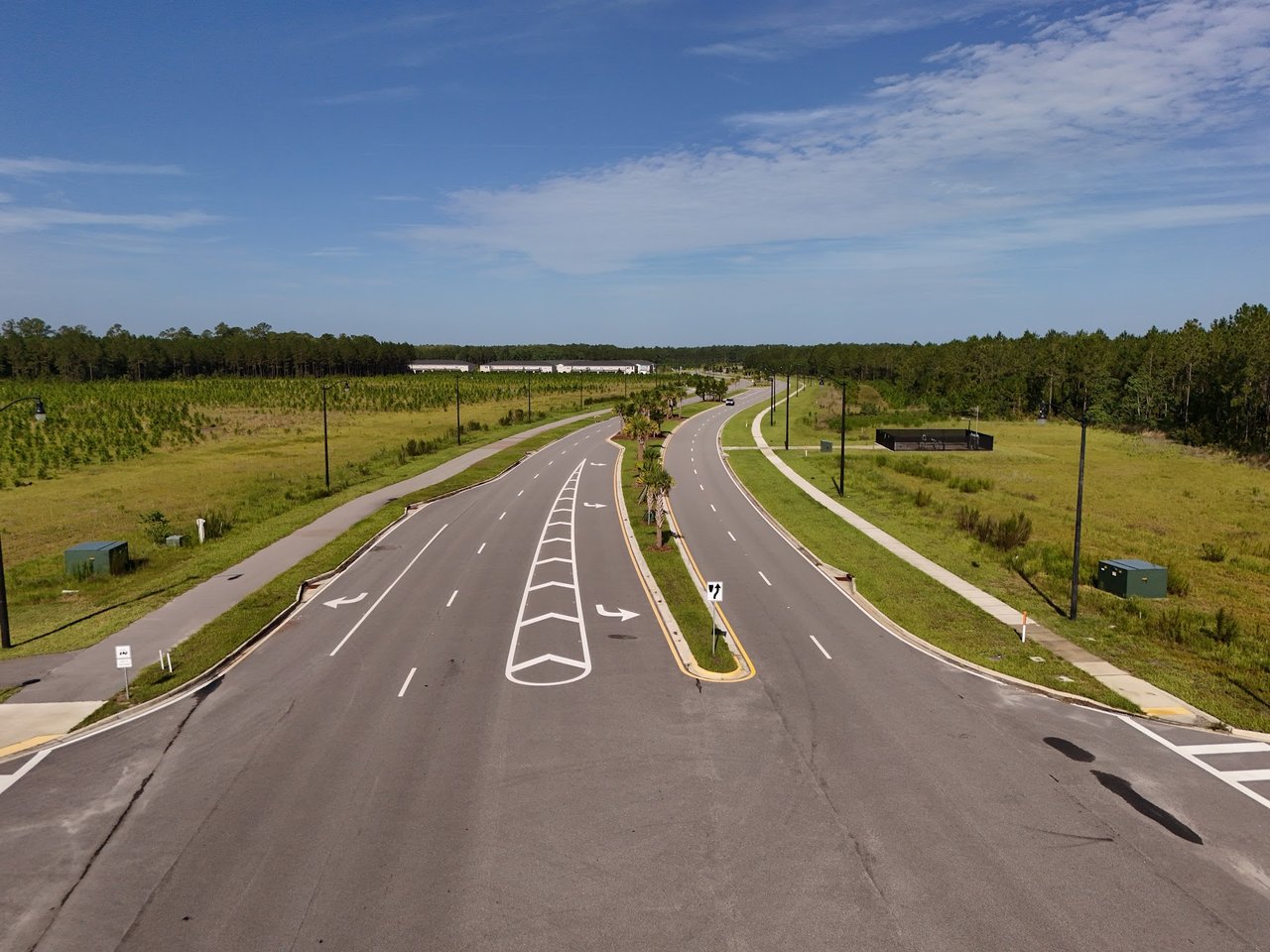 Divided neighborhood road with sidewalks, streetlights, and a landscaped median.