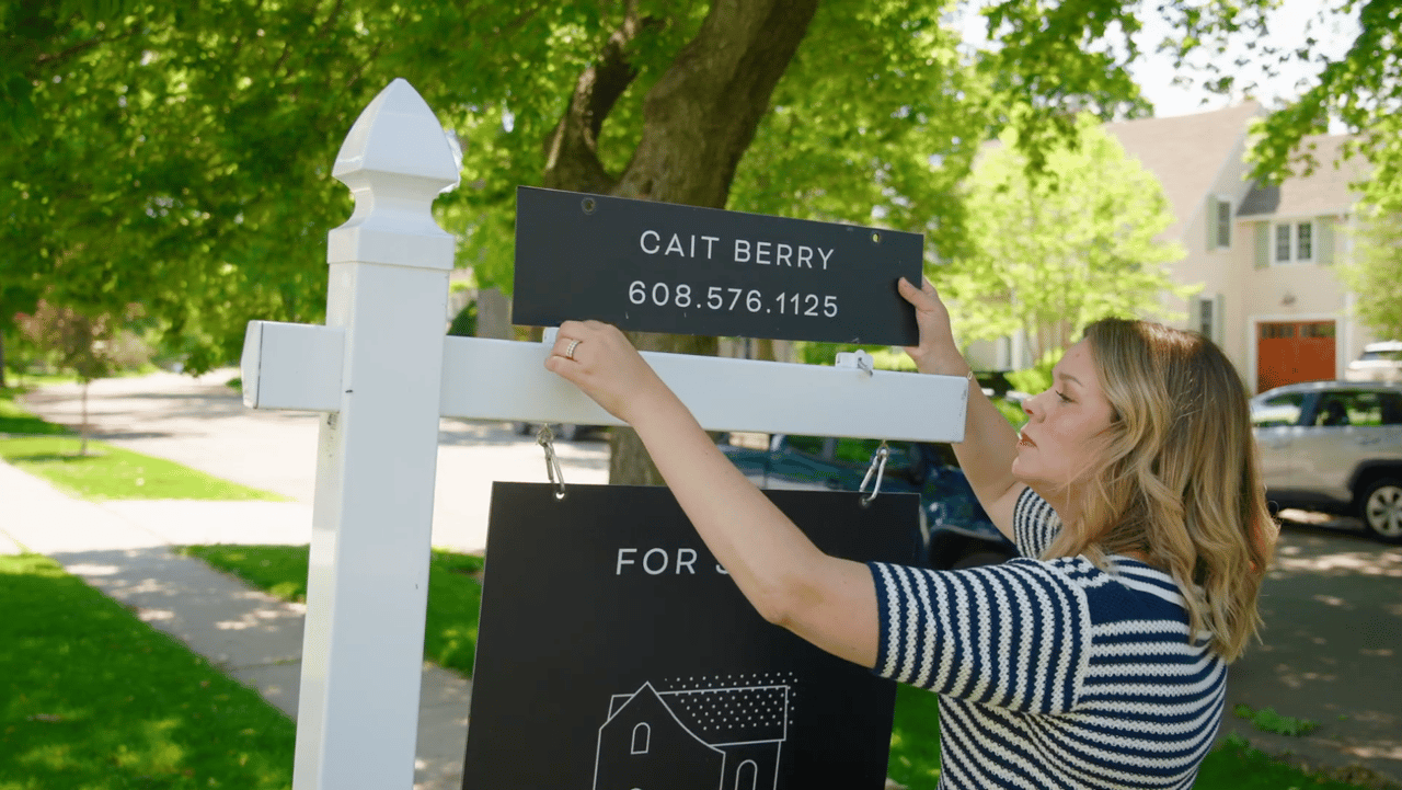 Cait Berry of Insiders Realty installing a For Sale sign on a tree-lined Madison neighborhood street, representing the surge in new home listings hitting the Dane County market this spring.