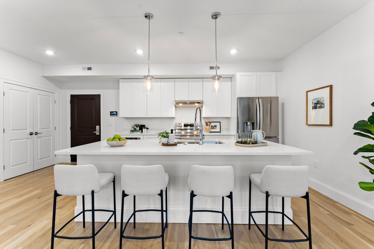 Bright white kitchen with a large island, four bar stools, and stainless steel appliances.