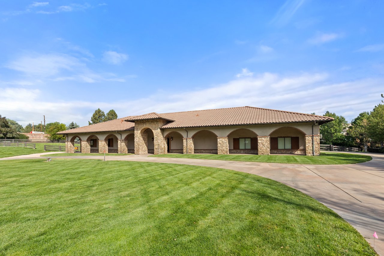 Equestrian barn with a tiled roof, stone arches, and a broad lawn.