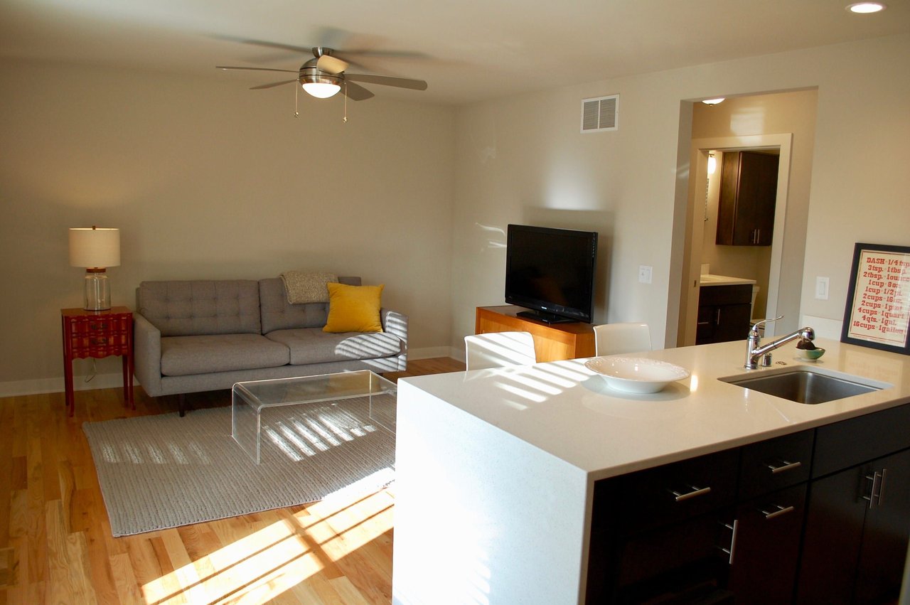 Open-plan apartment living room with a gray sofa beside a large kitchen island.