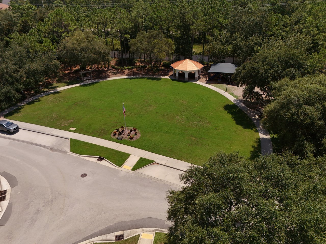 Neighborhood park with a broad lawn, flag, covered pavilion, and curving sidewalks.