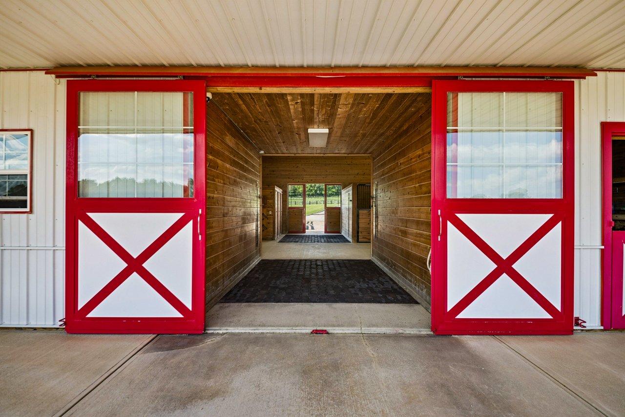 Red and white horse barn with center aisle opening to fenced pasture on a Central Ohio equestrian property.