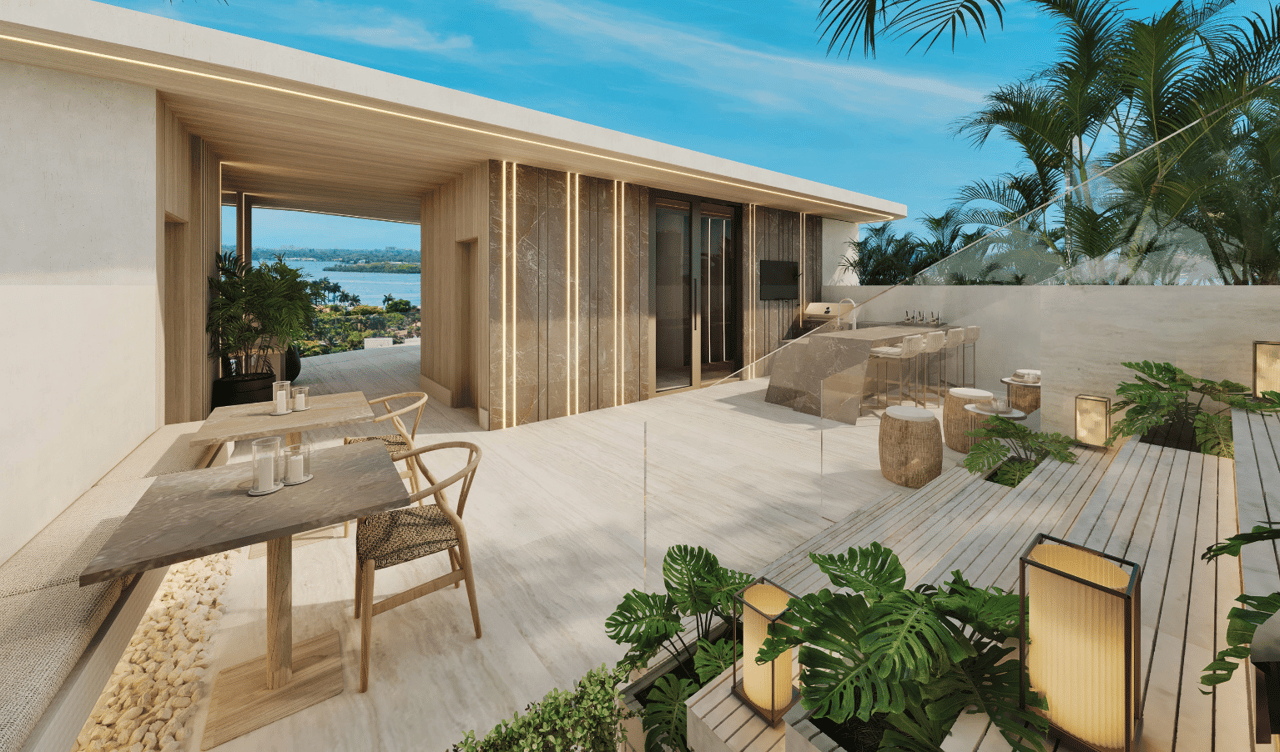 Waterfront condo terrace with outdoor dining, a built-in bar, tropical plants, and a bay view.