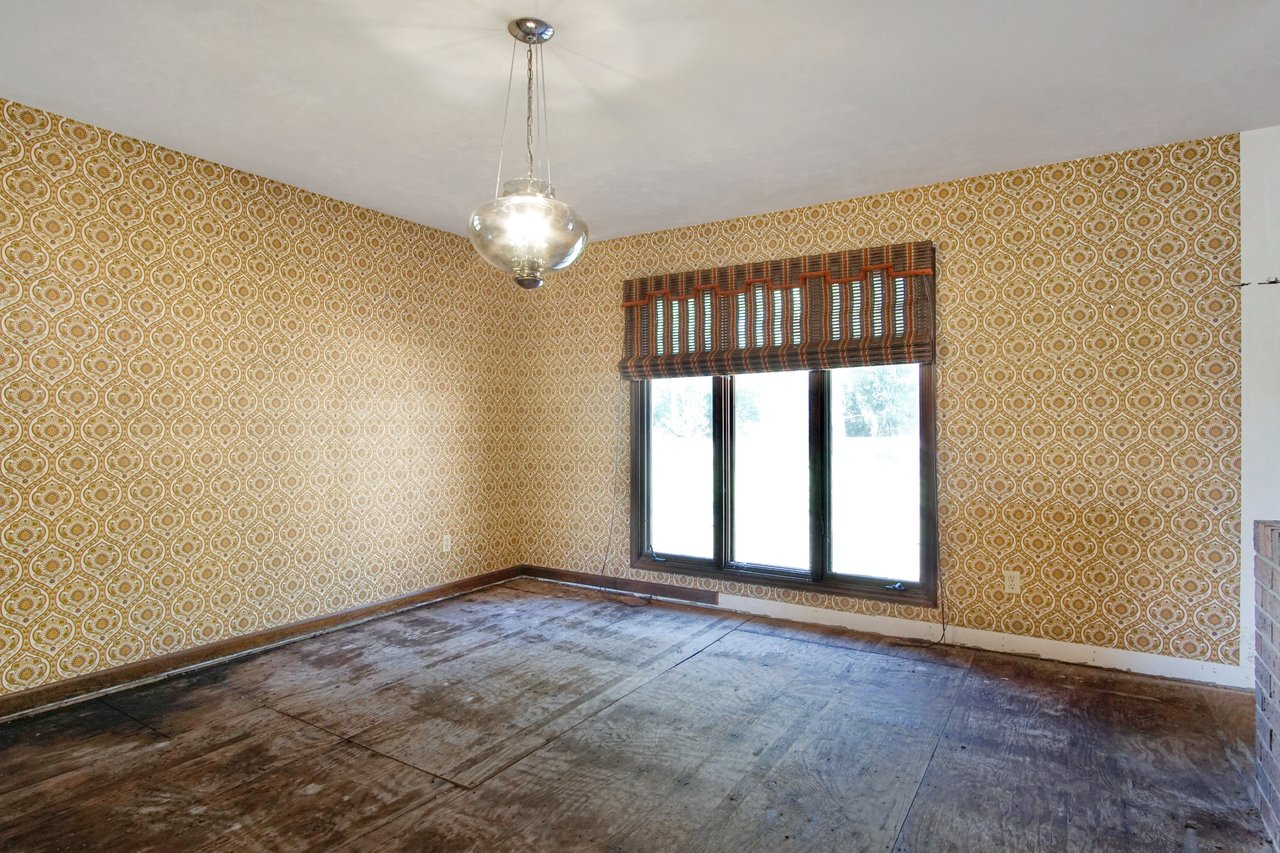 Empty room with vintage yellow patterned wallpaper, a three-panel window with striped curtains, and a retro hanging light fixture, conveying nostalgia.