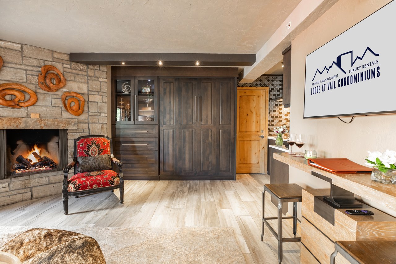 Condominium living area with a stone fireplace, dark cabinetry, and a red patterned armchair.