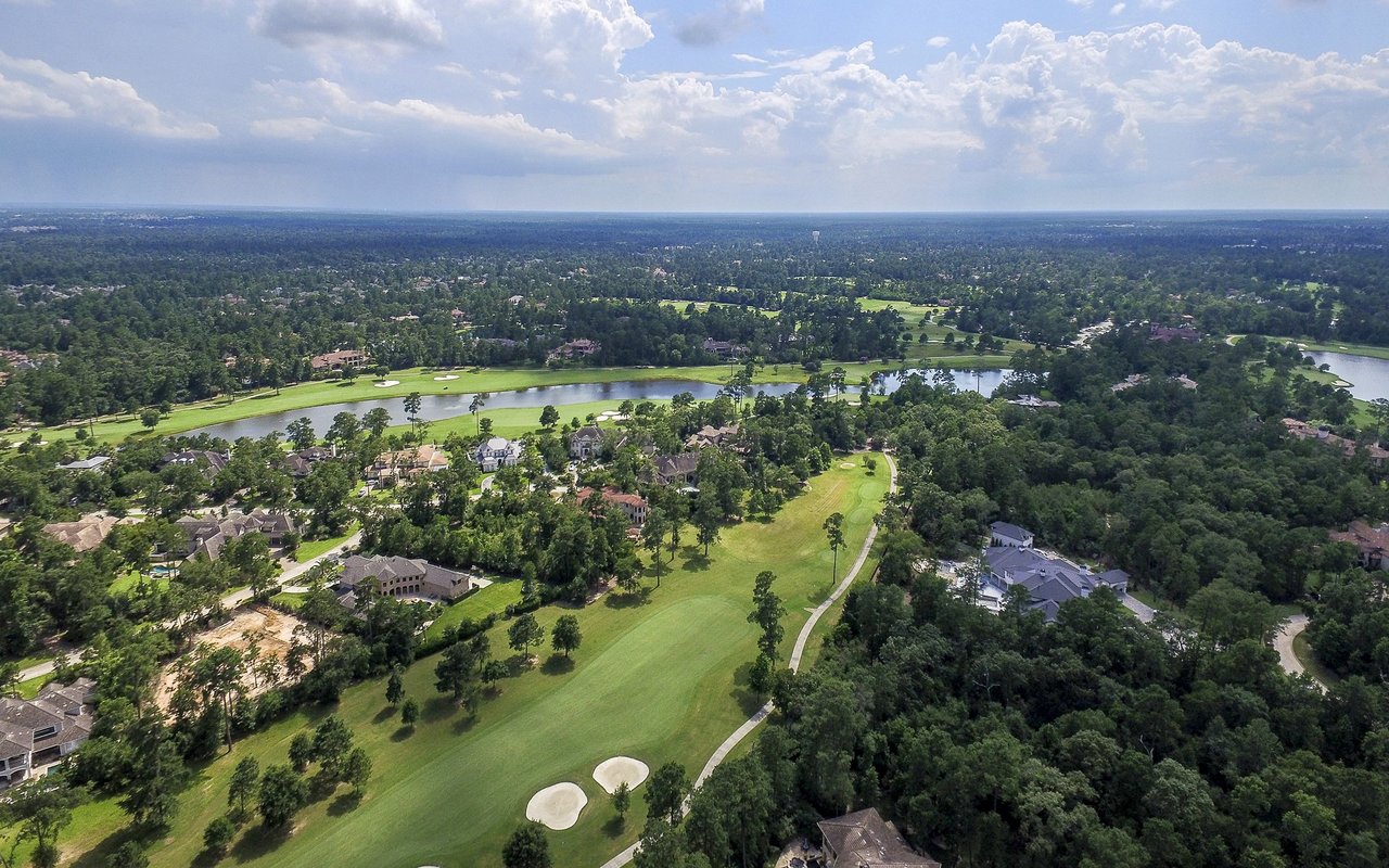 Aerial view of a golf course winding through a wooded residential neighborhood.