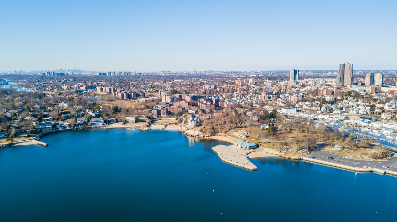 Aerial view of a waterfront neighborhood, marina, and distant city skyline.