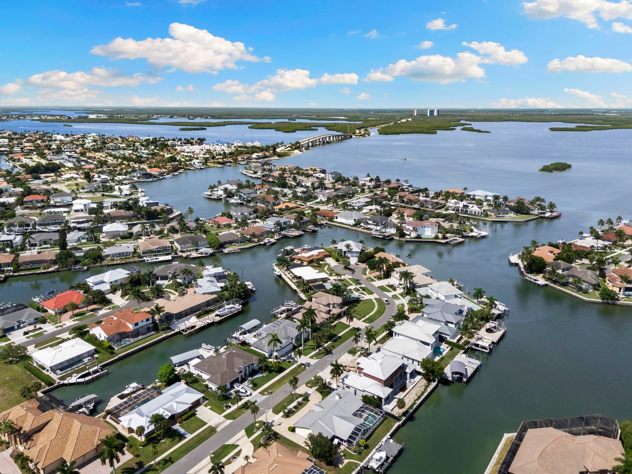 Aerial view of Marco Island waterfront homes, canals, private docks, and boats beside a broad bay.