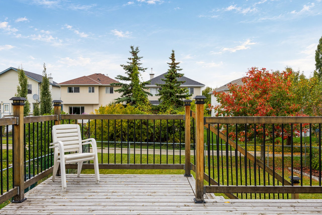 Backyard deck with black railings and a white chair overlooking autumn foliage and neighboring homes.