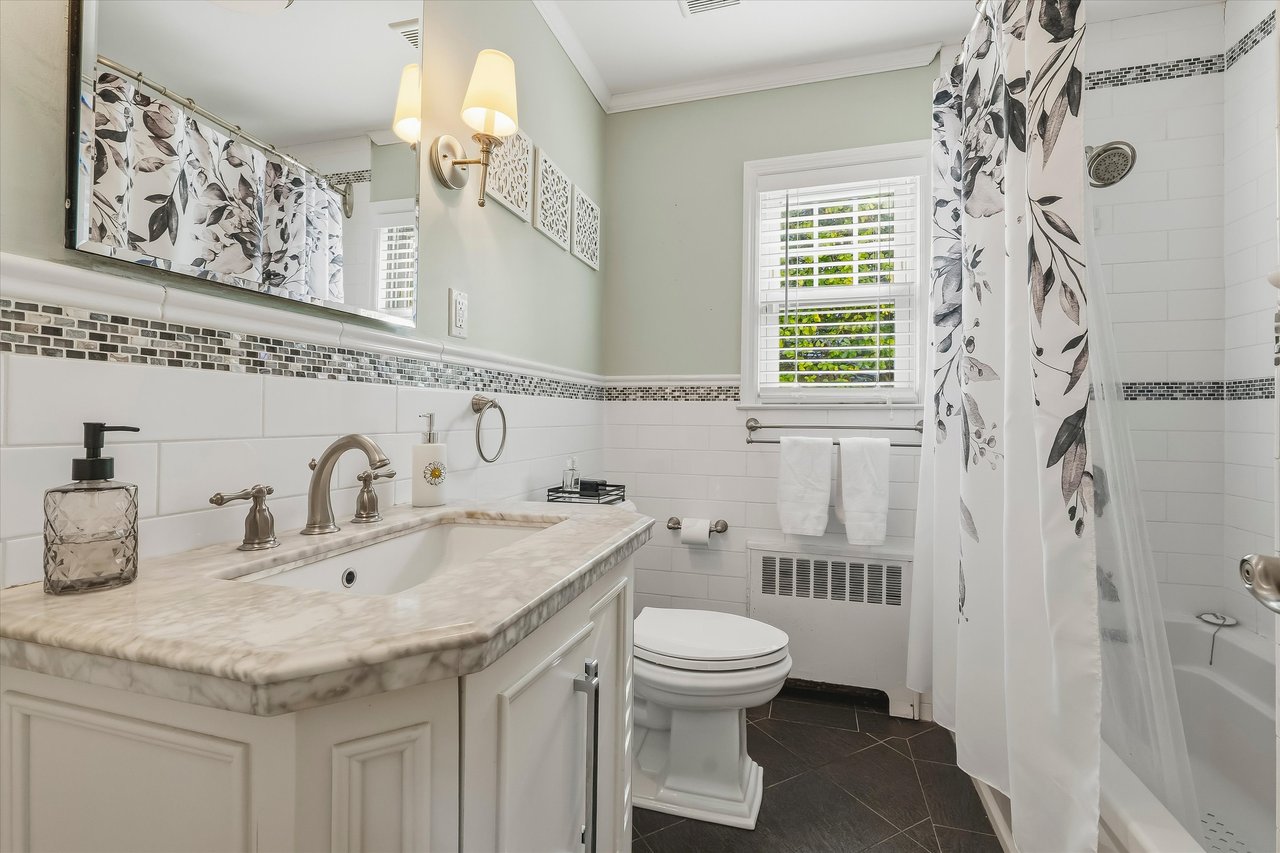 Bathroom with a marble-look vanity, dark tile floor, and floral shower curtain.