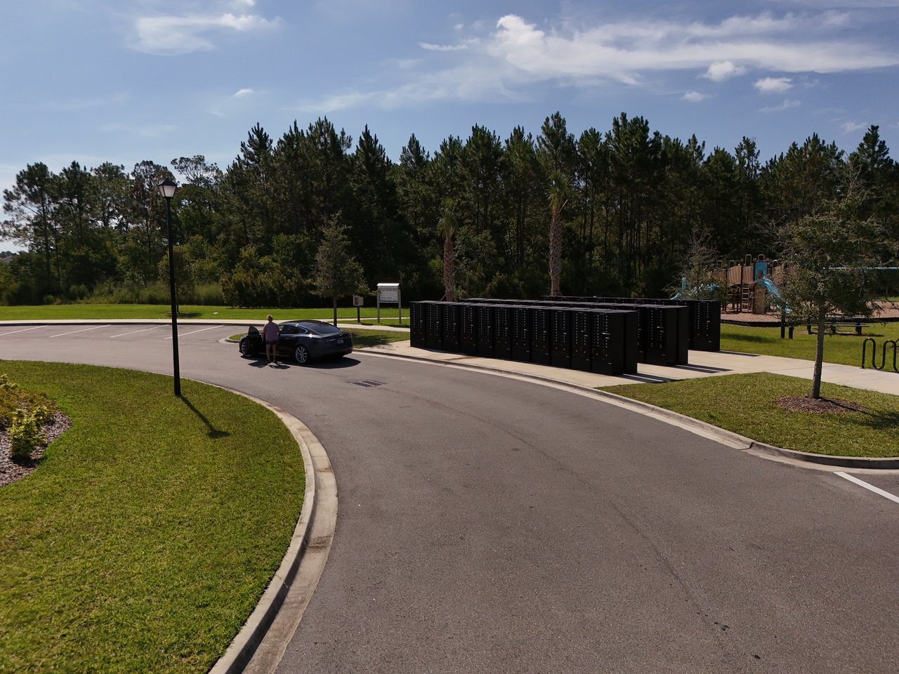 Community parcel lockers beside a paved drive, with a playground and trees behind them.
