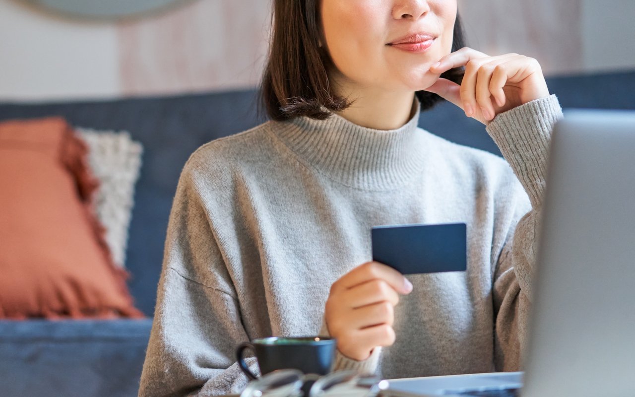 Woman considers a loan while holding a blue card beside her laptop.