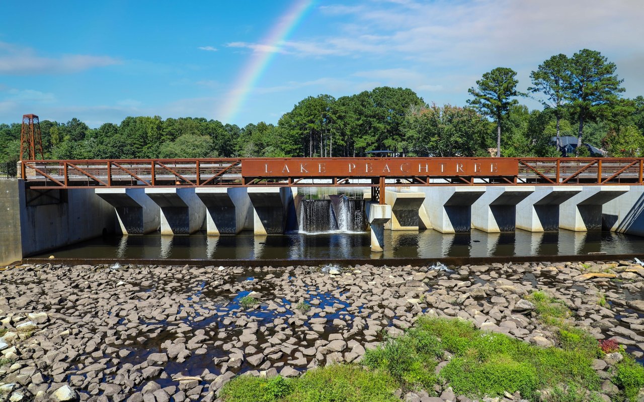 Lake Peachtree spillway and bridge beneath a rainbow, with the lake name displayed on the railing.