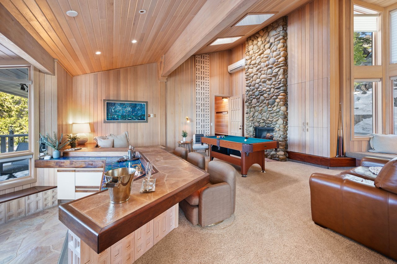 Wood-paneled great room with a stone fireplace, pool table, and long built-in counter.