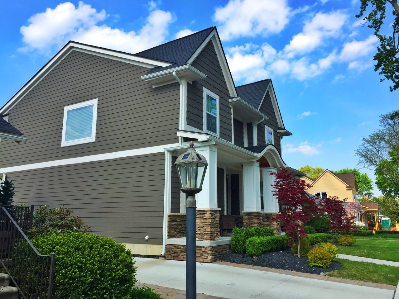 Gray two-story house with a stone-accented porch, landscaped yard, and neighboring homes.