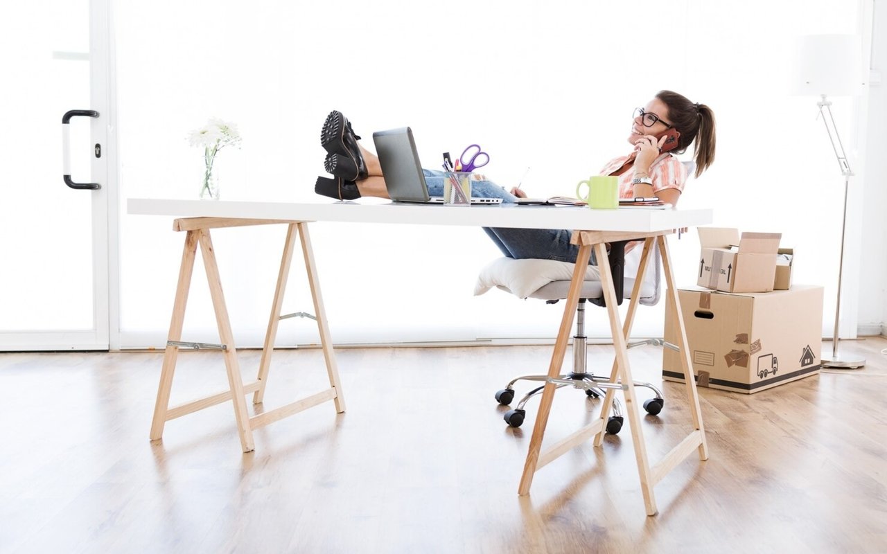 Woman talking on the phone at a home office desk beside moving boxes.