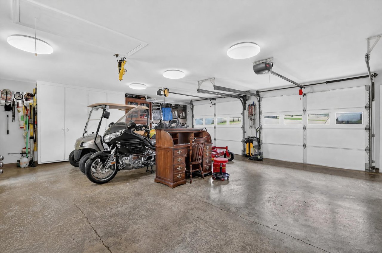Spacious garage with two overhead doors, a motorcycle, golf cart, and wooden desk.