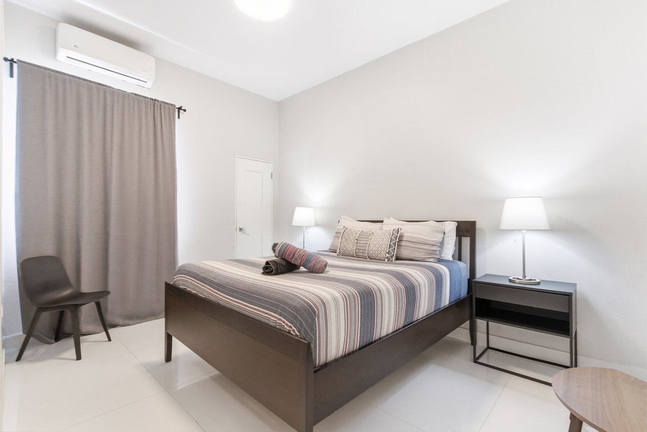 Furnished bedroom with striped bedding, gray curtains, and a wall-mounted air conditioner.