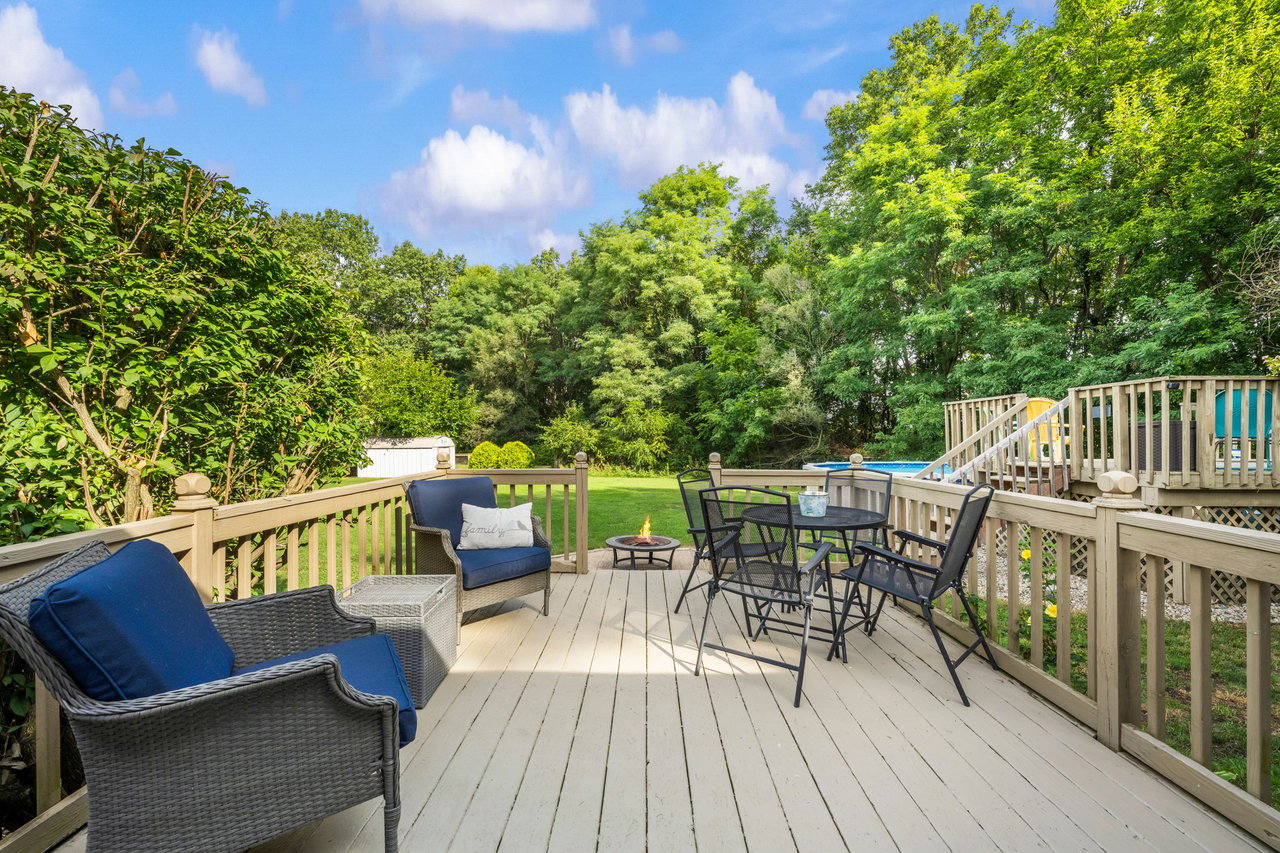 Furnished backyard deck overlooking a lawn and pool, with lounge chairs and a fire pit.