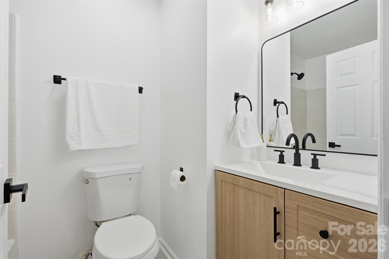 Modern bathroom with a light wood vanity, black fixtures, large mirror, and white toilet.