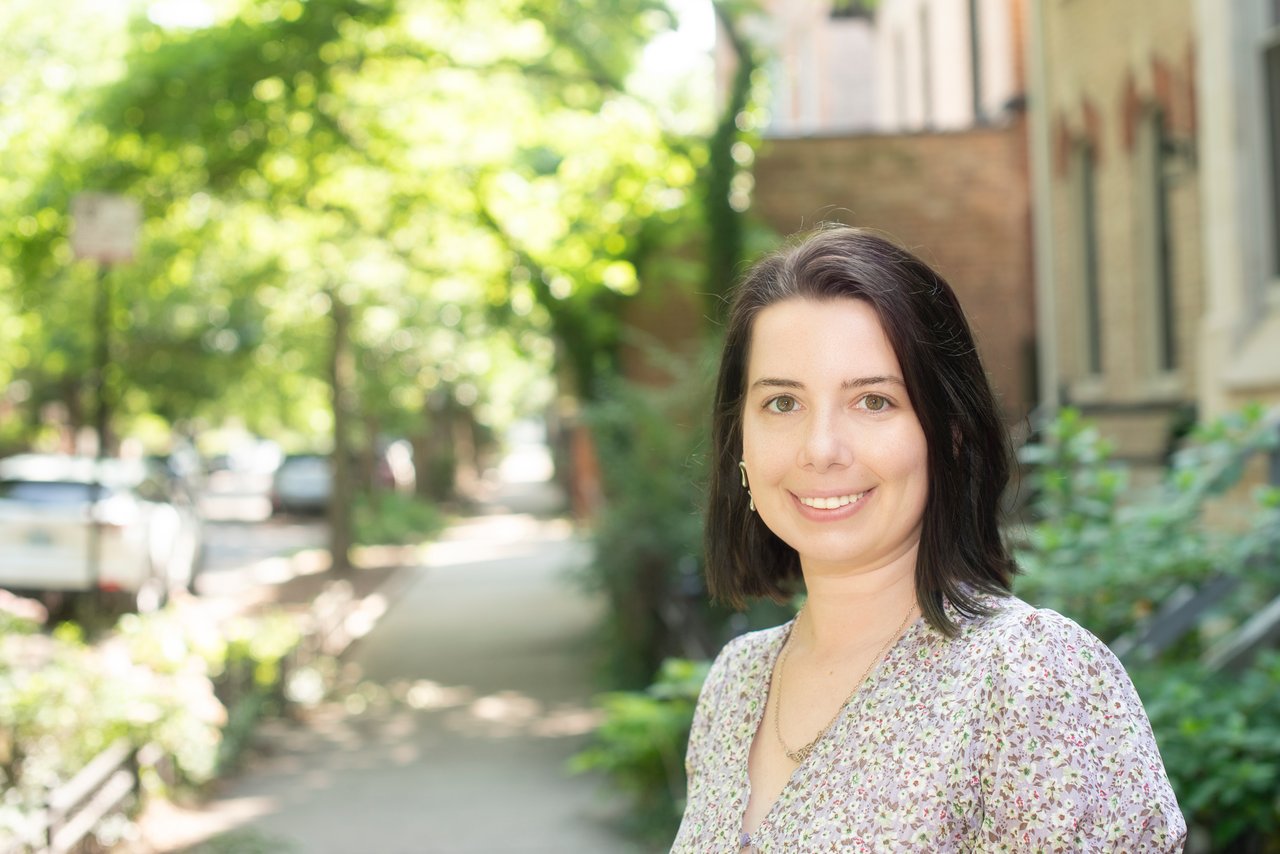 Eliza Couvillion smiling outdoors on a leafy, tree-lined sidewalk.