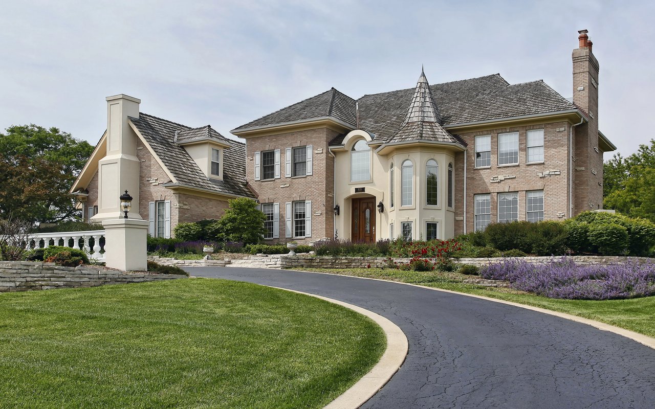 Two-story brick house with a turret, landscaped gardens, and a curved driveway.