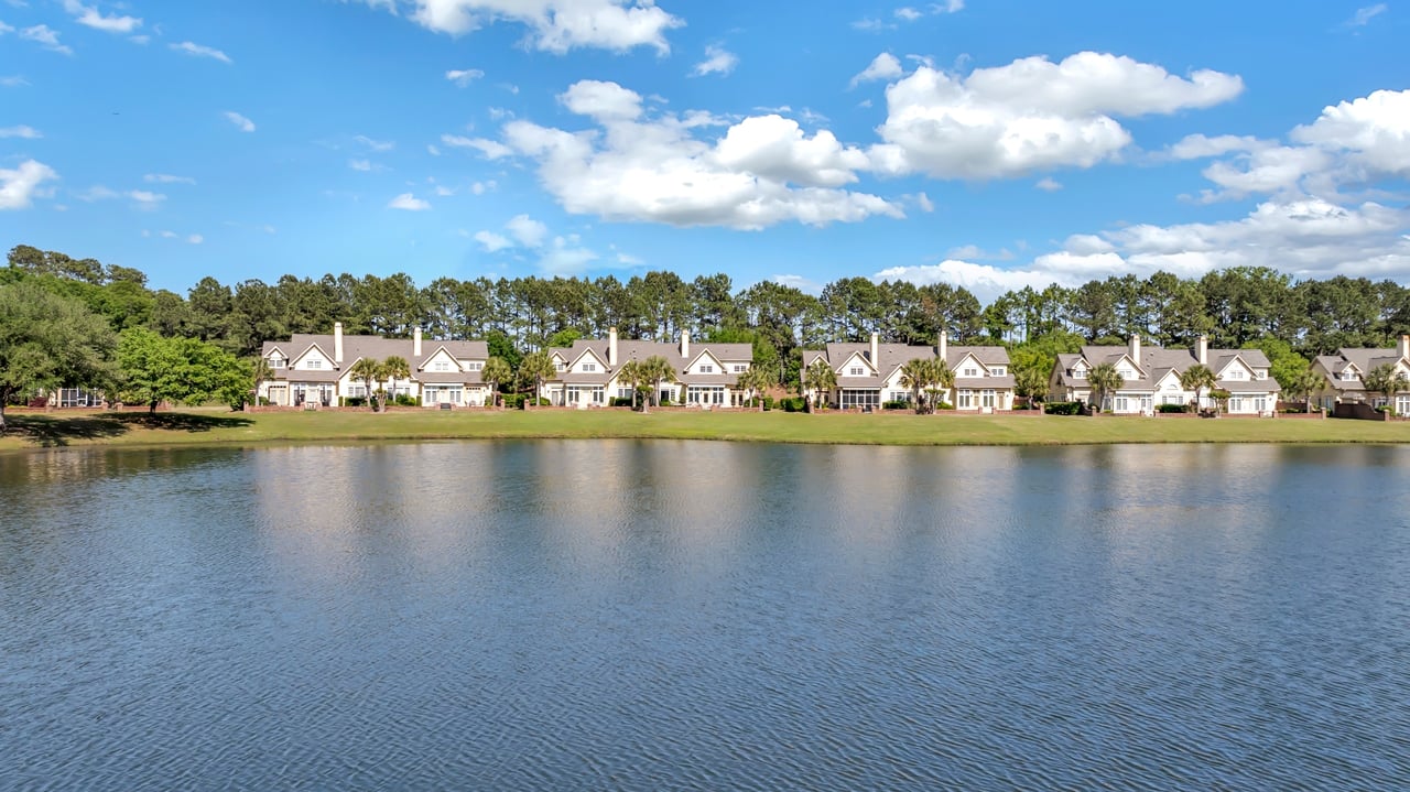 Lakefront villas across the water, backed by trees beneath a partly cloudy sky.