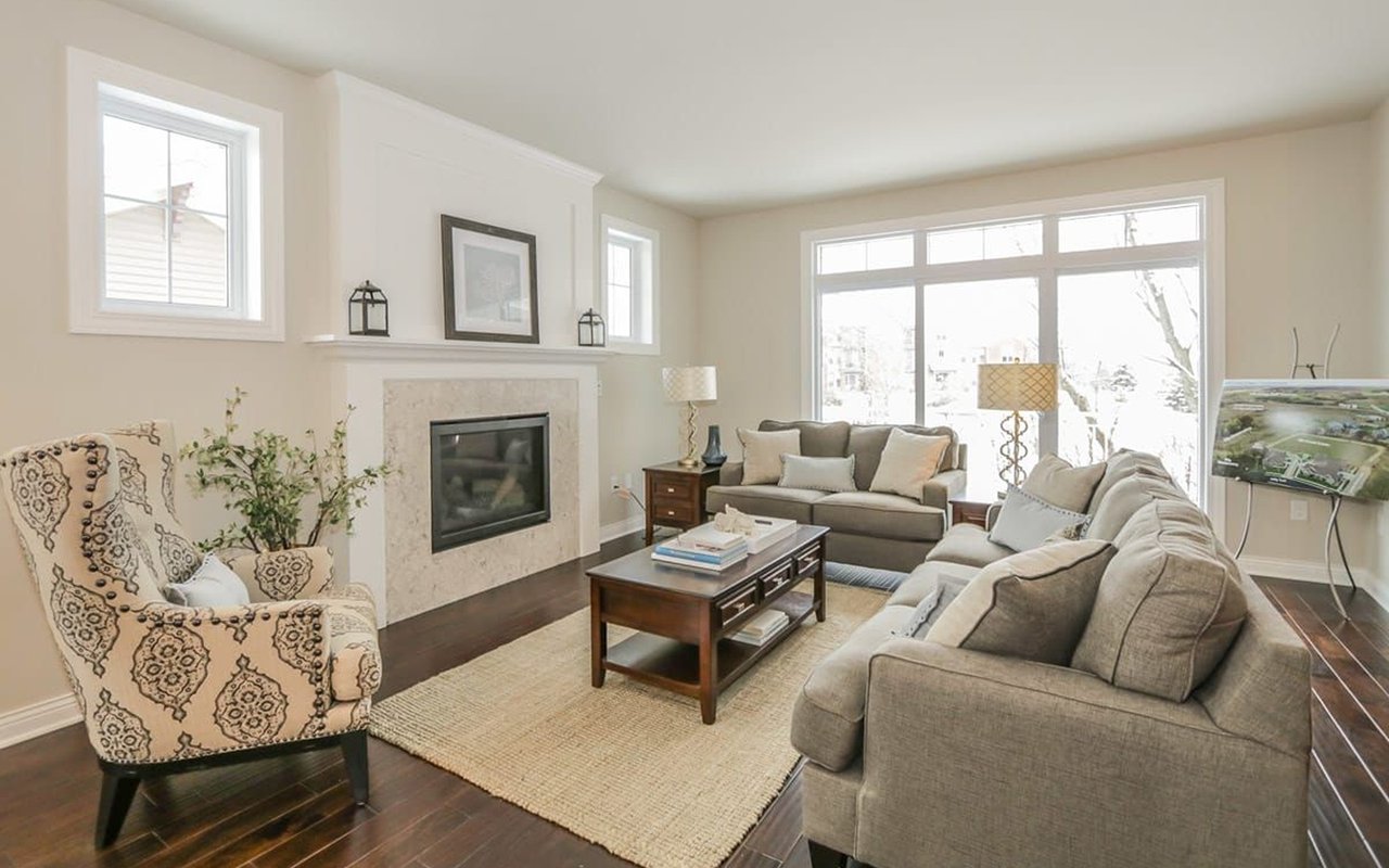 Staged living room with a stone fireplace, gray sofas, and large windows overlooking snow.