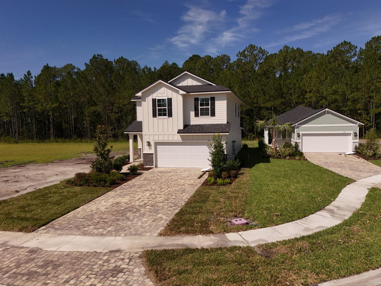 Two-story home with dark shutters and a brick-paver driveway, beside a smaller single-story home.