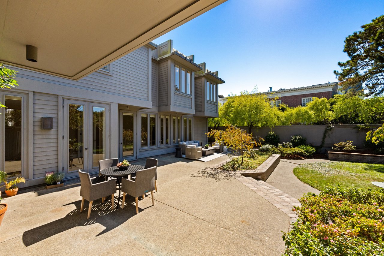 House with a spacious paved patio, outdoor dining set, lounge seating, and landscaped garden.