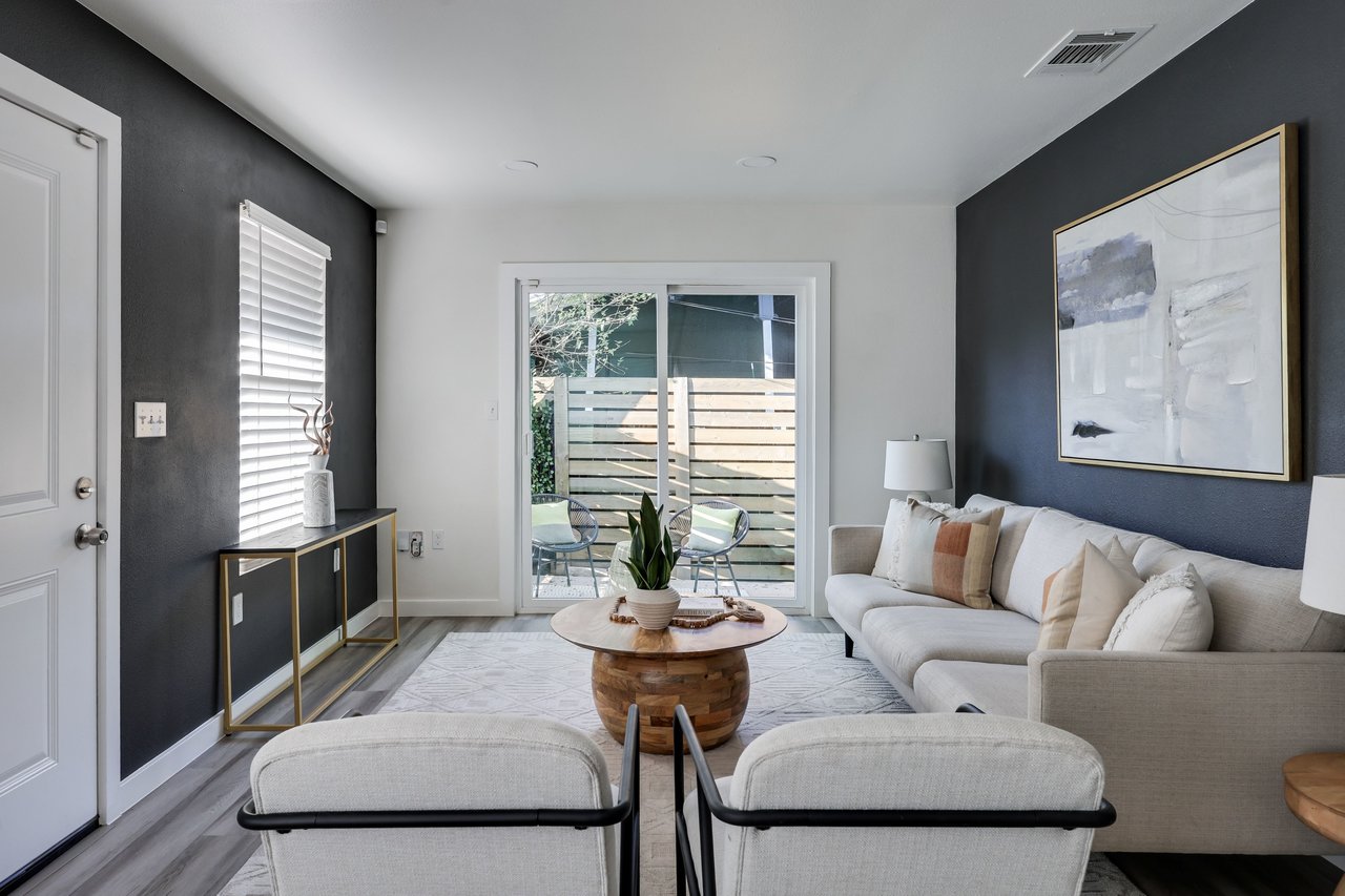 Staged living room with a light sectional, round wood coffee table, and sliding doors to a fenced patio.