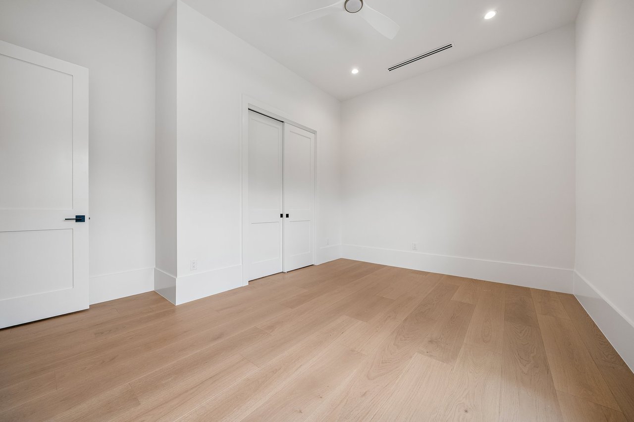 Empty room with light wood floors, double closet doors, and a ceiling fan.