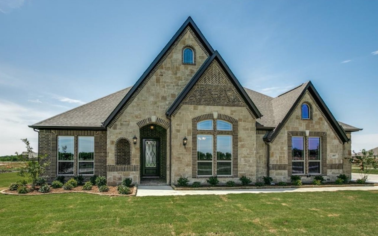 Stone-and-brick home with steep gables, arched entry details, and a broad green lawn.