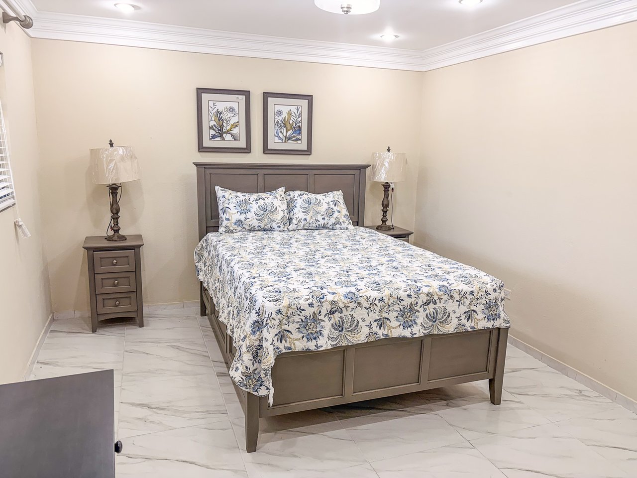Bedroom with blue-and-white floral bedding, dark wood furniture, and marble-look tile flooring.