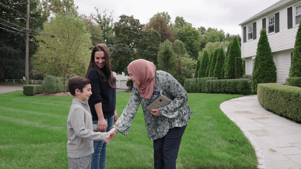 Noora Brown shaking hand with a boy and his mon in front of a house
