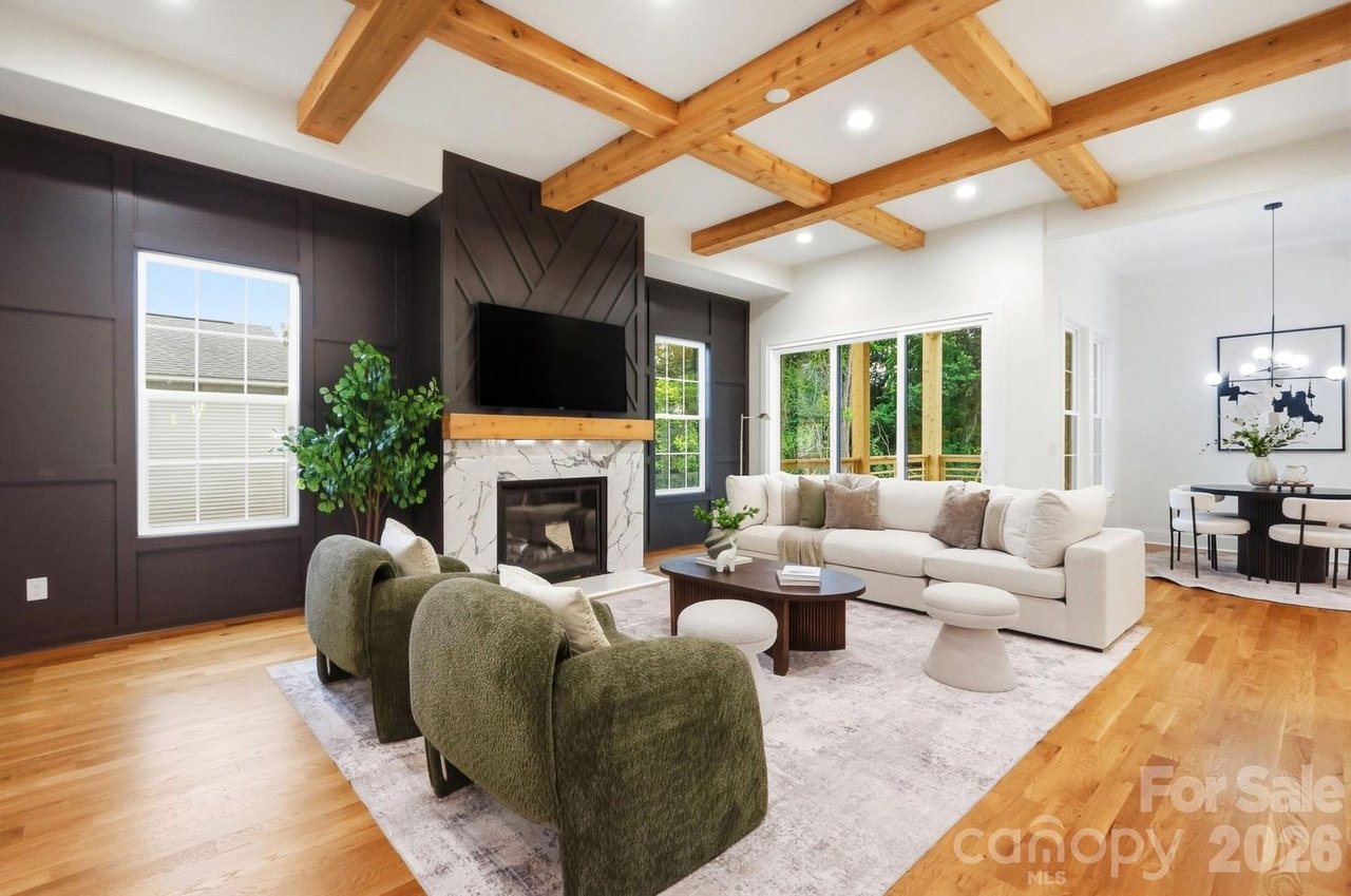 Living room with exposed timber beams, a dark fireplace wall, cream sectional, and green chairs.