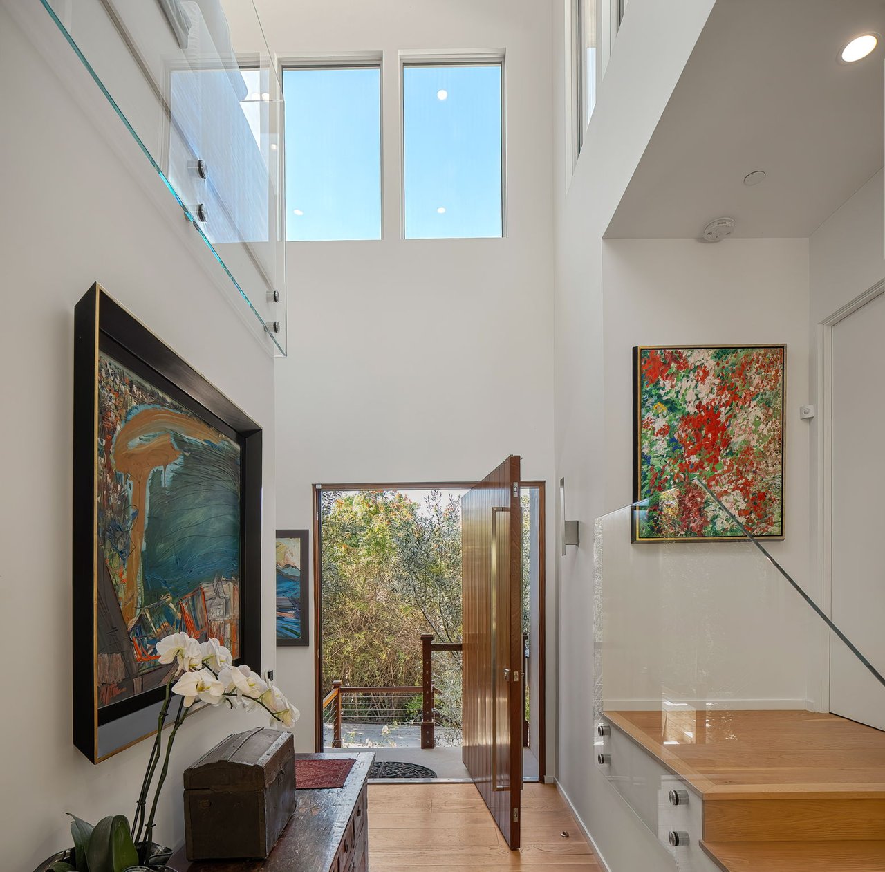 Double-height entry foyer with a glass-railed staircase and an open front door.