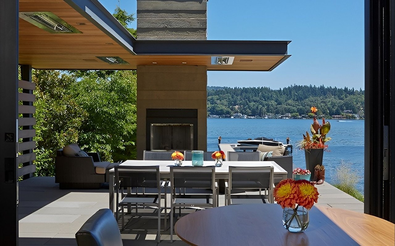 Lakeside patio with modern dining furniture, a built-in fireplace, and views across the water.