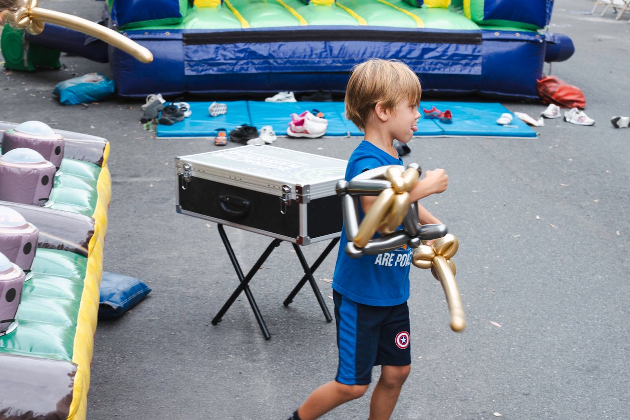 Child carrying a gold balloon animal beside inflatable play equipment.
