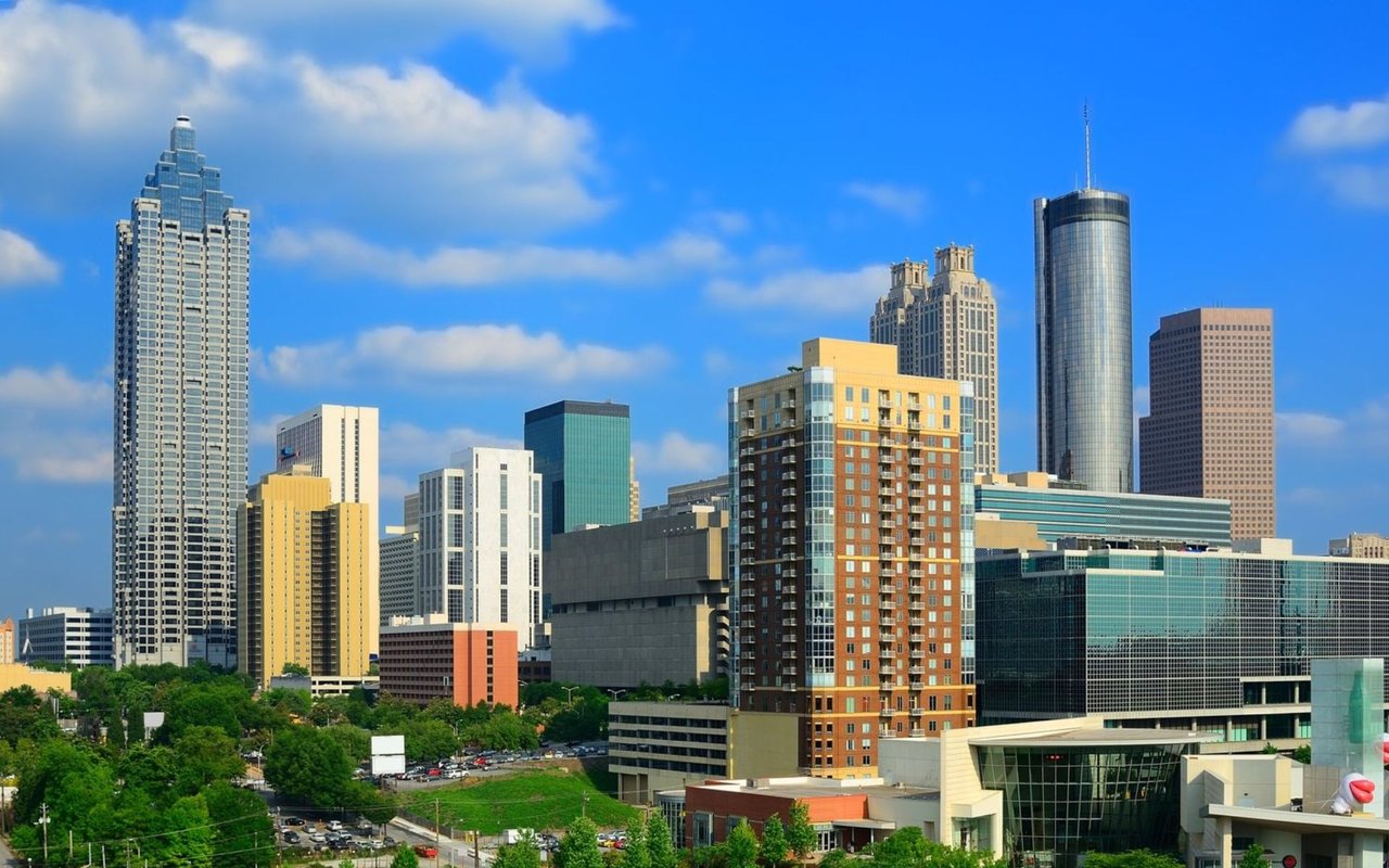 Downtown skyline of modern high-rise buildings beneath a bright blue, partly cloudy sky.