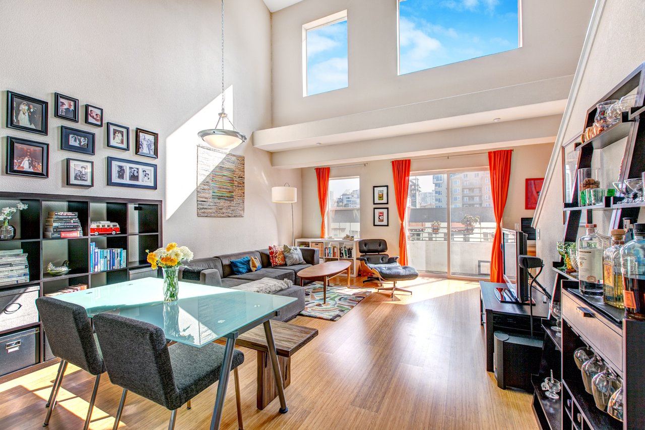 Bright loft living room with high ceilings, orange curtains, and a glass dining table.