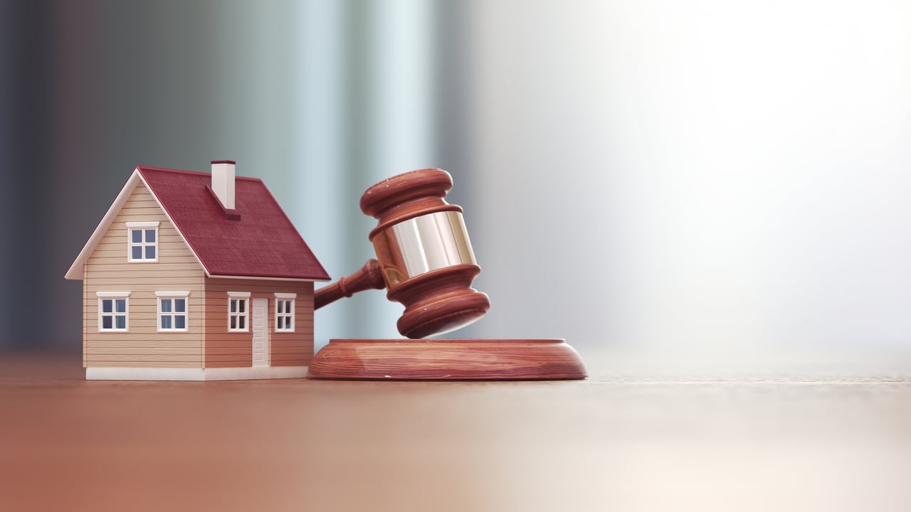 A small wooden house model beside a wooden judge’s gavel resting on its base, symbolizing property law, real estate regulation, or landlord-tenant legal issues.