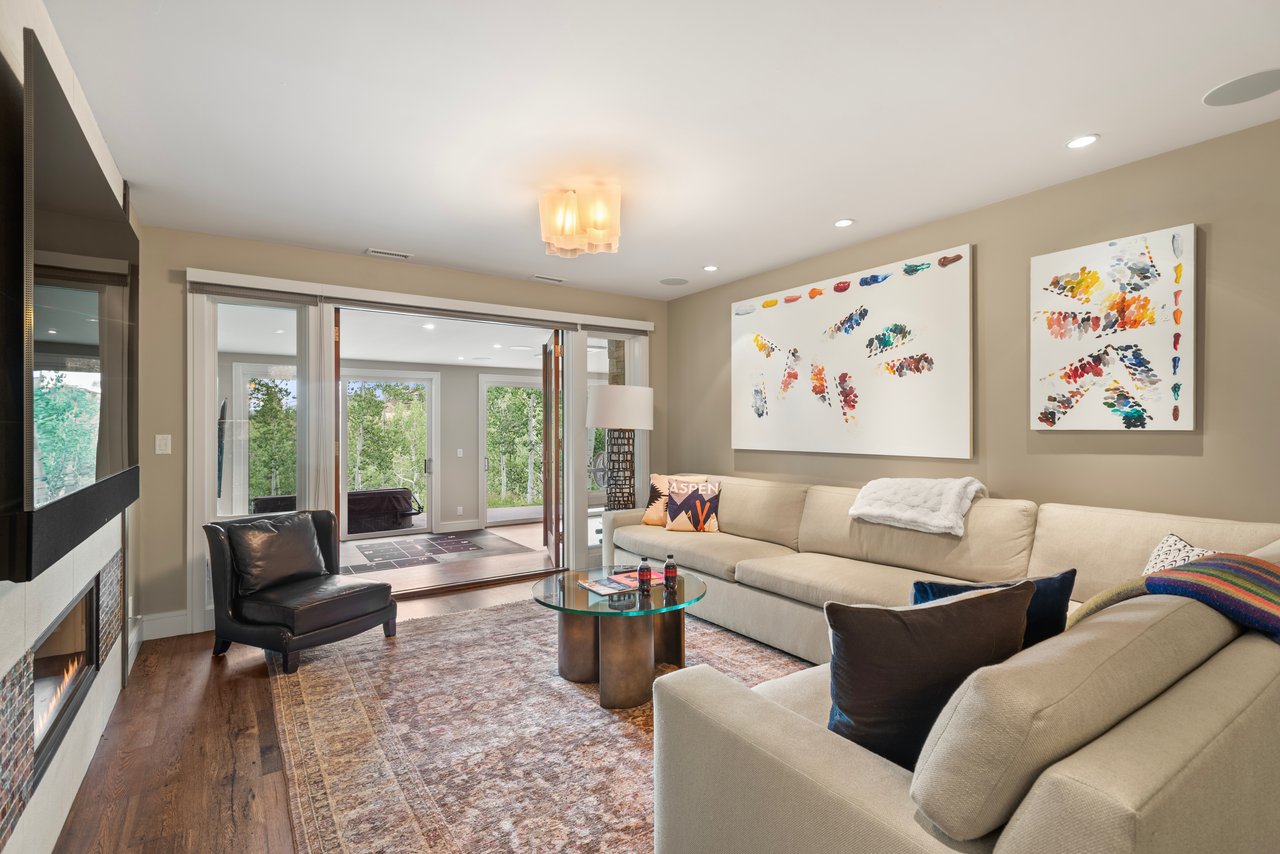 Living room with a beige sectional, fireplace, abstract artwork, and sliding glass doors to a leafy patio.