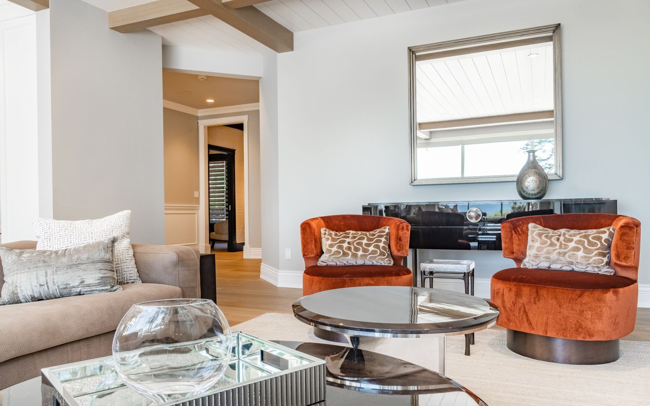 Living room with rust-orange armchairs, a beige sofa, and exposed wood ceiling beams.