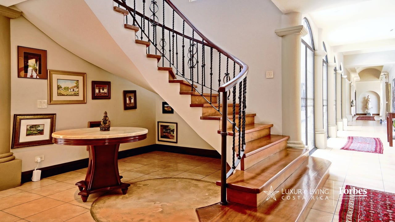 Foyer with a curved wooden staircase, black iron railing, framed artwork, and a round console table.